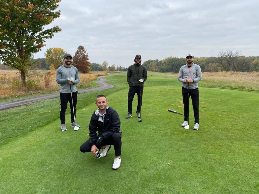 Four alumni posing on golf course